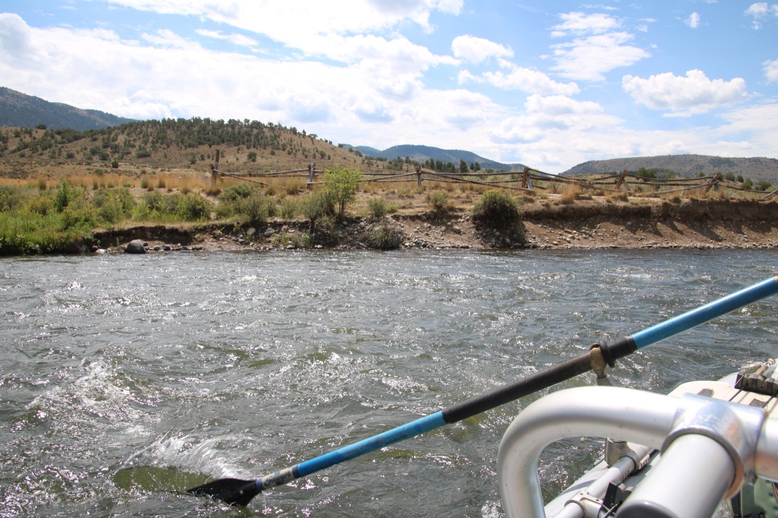 View from a drift boat looking across the Upper Colorado River toward a split-rail fence and hills